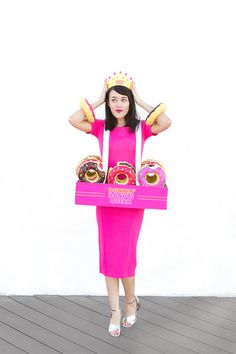 a woman in a pink dress is holding a box with donuts on it and wearing a crown