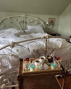 a tray with cups and tea on it in front of a white iron bed frame