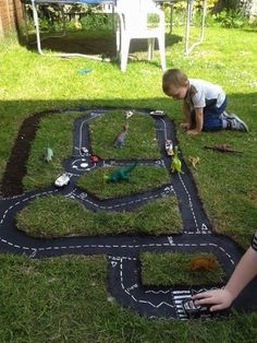 a young boy playing in the grass with his toy train set and cars on it