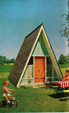 two children are playing in the grass near a small house with a roof that is shaped like a tent