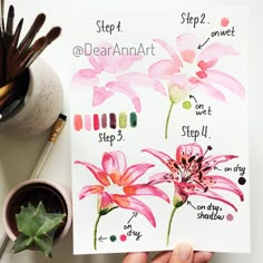 a person holding up a card with watercolors on it and flowers in the background