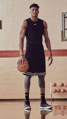 a man holding a basketball while standing on top of a gym floor in front of a ball