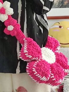 a pink and white crocheted bag with flowers hanging from it's handle