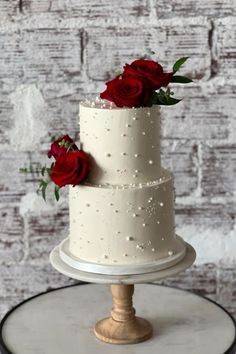 a three tiered white cake with red roses on top