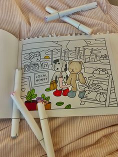 an open coloring book sitting on top of a bed next to two markers and pens