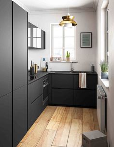 a kitchen with black cabinets and white walls, wood floors and a gold pendant light hanging over the sink