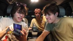 three young men sitting in the back of a car looking at a cell phone screen