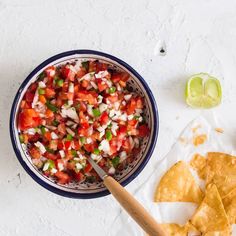 a bowl filled with salsa next to tortilla chips and lime wedges on a white surface