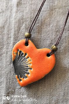 an orange and black heart shaped pendant on a brown cord