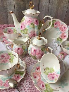 a tea set with pink flowers and gold trimmings sits on a tablecloth