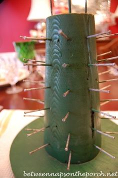 a green vase with pins sticking out of it's sides sitting on a table