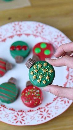 someone is holding up some decorated cookies on a white plate with red, green and gold decorations