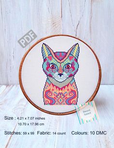 a cross - stitch cat is shown on a white wooden surface with a tag in front of it