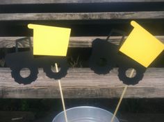 two yellow construction vehicles on sticks in a metal bowl next to a wooden bench with grass