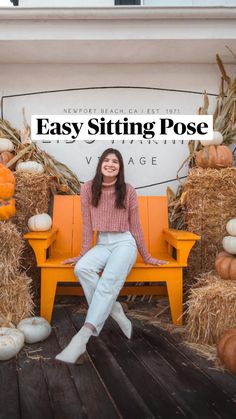 a woman sitting on an orange bench in front of hay bales and pumpkins