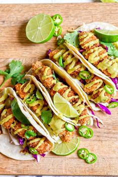 three tacos with limes and cilantro on a cutting board