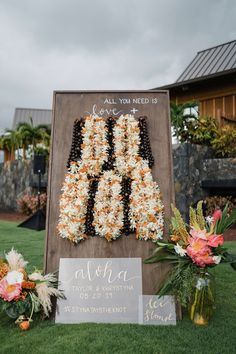 a sign that has flowers on it in front of some grass and plants with the words, all you need is aloha