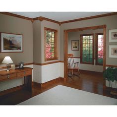 a living room with wood trimming and two windows on the wall, along with a white rug