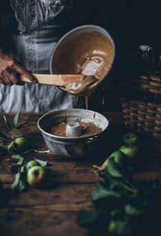 a person pouring something into a bowl on top of a wooden table next to apples