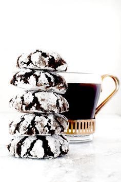 a stack of cookies next to a cup of coffee on a white counter top with powdered sugar