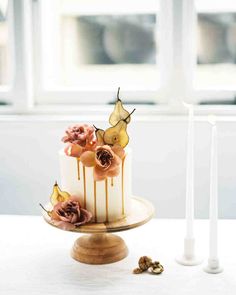 a three tiered cake with flowers and candles on a table in front of a window