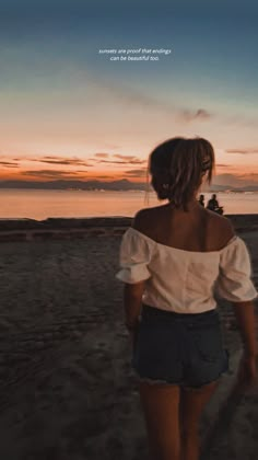 a woman standing on top of a sandy beach next to the ocean at sunset or dawn