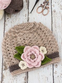 a crocheted hat with flowers on it next to some yarn and scissors in the background