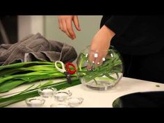 a woman is arranging flowers in a vase on a table with glasses and napkins