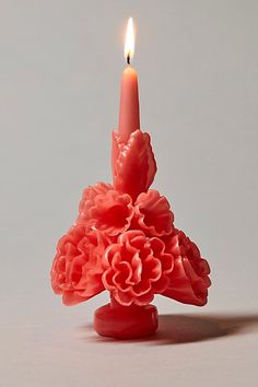 a red candle with a pink flower on it's side and a lit candle in the middle