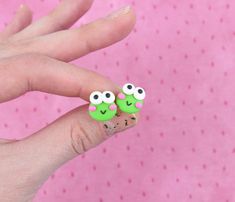 a person's hand holding two green and pink earrings with googly eyes on them