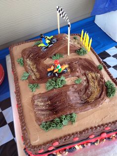 a birthday cake that is shaped like a dirt bike track with cars on the track