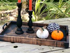 three pumpkins and two candles are on a wooden tray with some black candle holders