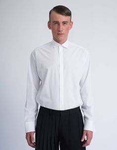 This minimal designed shirt has an emphasis on silhouette, it has a roomy shape enhanced by the dropped shoulder seams and squared hem. It has a two piece sleeve with a deep placket detailed with a fine contrasting gross grain ribbon. The exaggerated sleeves proportions give this oversized shirt it's modern and edgy look. This shirt is made from a crisp white cotton poplin and would easily become your wardrobe key item. It’s the perfect piece to dress an outfit up or down with minimal effort - i Modern Office Shirt With Concealed Placket, Formal Shirt With Cuffed Sleeves And Fold Down Collar, Modern Formal Shirt With Concealed Placket, Modern Formal Shirt With Fold Down Collar, Modern Semi-formal Shirt With Button Cuffs, Modern Shirt With Concealed Placket For Business Casual, Modern Office Shirt, Modern Semi-formal Shirt With Hidden Buttons, Tailored Modern Shirt For Semi-formal Occasions