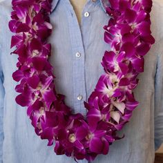 a man wearing a blue shirt and purple orchid leis around his neck is standing in front of a white wall