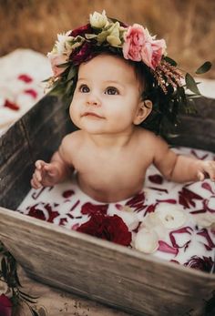 a baby wearing a flower crown sitting in a wooden box with flowers on it's head