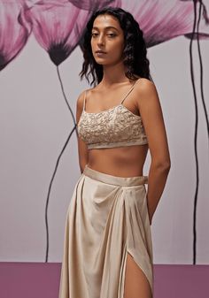 Step into a world of sophistication with our chic nude gold pleated skirt, made from luxurious satin fabric that cascades gracefully, accentuated by a tasteful slit for that hint of allure. Complementing this is a delicate net blouse, intricately hand-embroidered to infuse a dash of glamour. The ensemble is beautifully completed with a chiffon cape, elegantly adorned with handcrafted embellishments. This stunning indo western set is ideal for making a memorable statement at cocktail or sangeet p Gold Pleated Skirt, Blouse Satin, Cape Set, Chiffon Cape, Net Blouse, Skirt Satin, Net Blouses, Vacuum Storage, Ready To Wear Saree