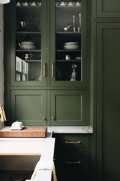 a kitchen with green cupboards and white counter tops in the center, along with dishes on wooden cutting board