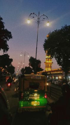 a green truck driving down a street next to a tall clock tower