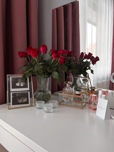 a white table topped with vases filled with red roses next to a window covered in curtains