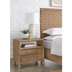 a nightstand with a lamp on it next to a bed and a white brick wall