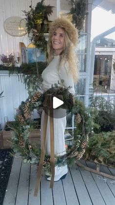 a woman holding a wreath on top of a wooden floor next to potted plants