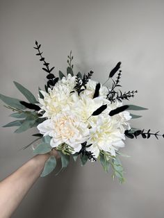 a bouquet of white flowers is held by a person's hand in front of a gray wall