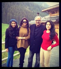 three people standing next to each other in front of a building with mountains behind them