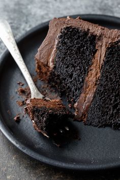 a piece of chocolate cake on a black plate with a fork and spoon next to it