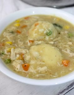 a white bowl filled with chicken and dumpling soup on top of a wooden table