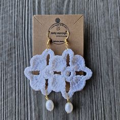 two white crochet earrings with pearls hanging from them on a piece of wood