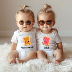 two toddlers wearing matching shirts and sunglasses sitting next to each other on a white rug