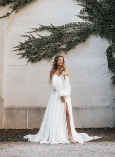 a woman in a white dress standing next to a wall with greenery on it