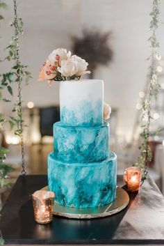 a three tiered cake with blue and white frosting on a table next to candles