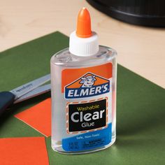 a bottle of clear glue next to a pair of scissors on top of a table